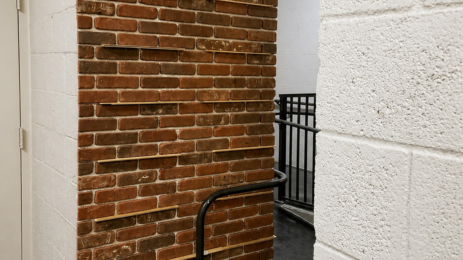 Custom brick-and-wood horizontal-shelf feature wall in a residential lower-level corridor with steel railing beyond.