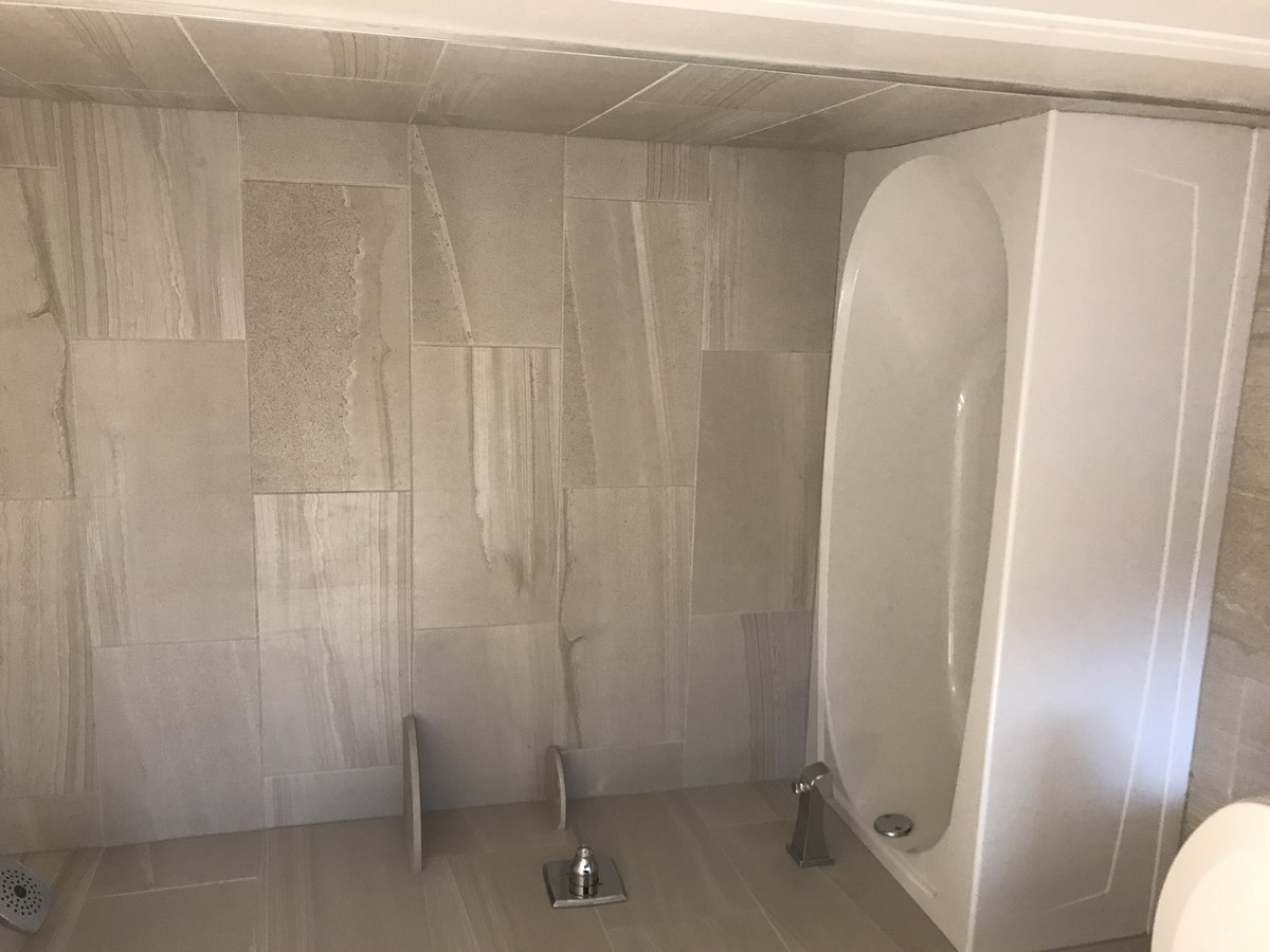 Tub-and-shower wall finished in large-format porcelain tile with grey marbling, soaking tub and modern fixtures, accent corner shelf.