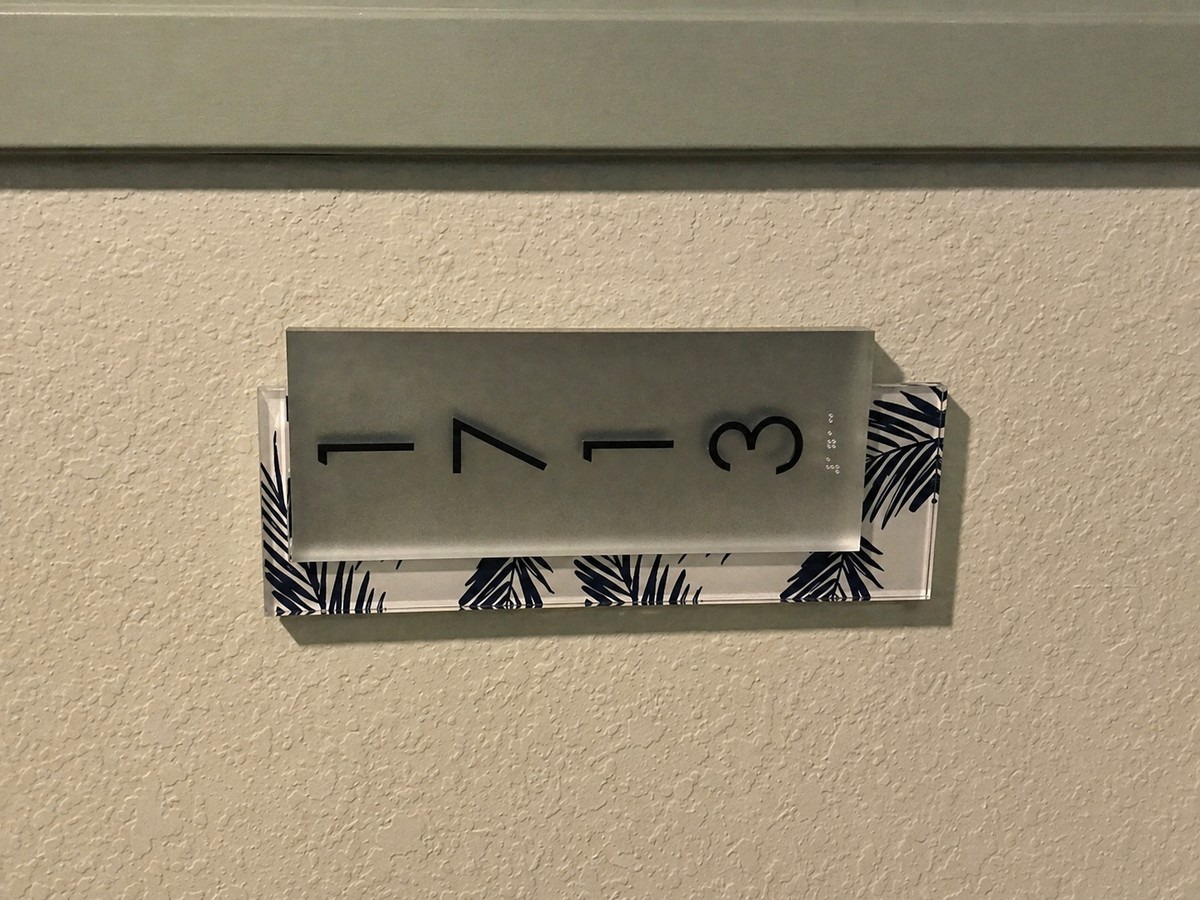 Condo unit 173 number plaque with frosted glass and palm-leaf decorative backing, hallway context.