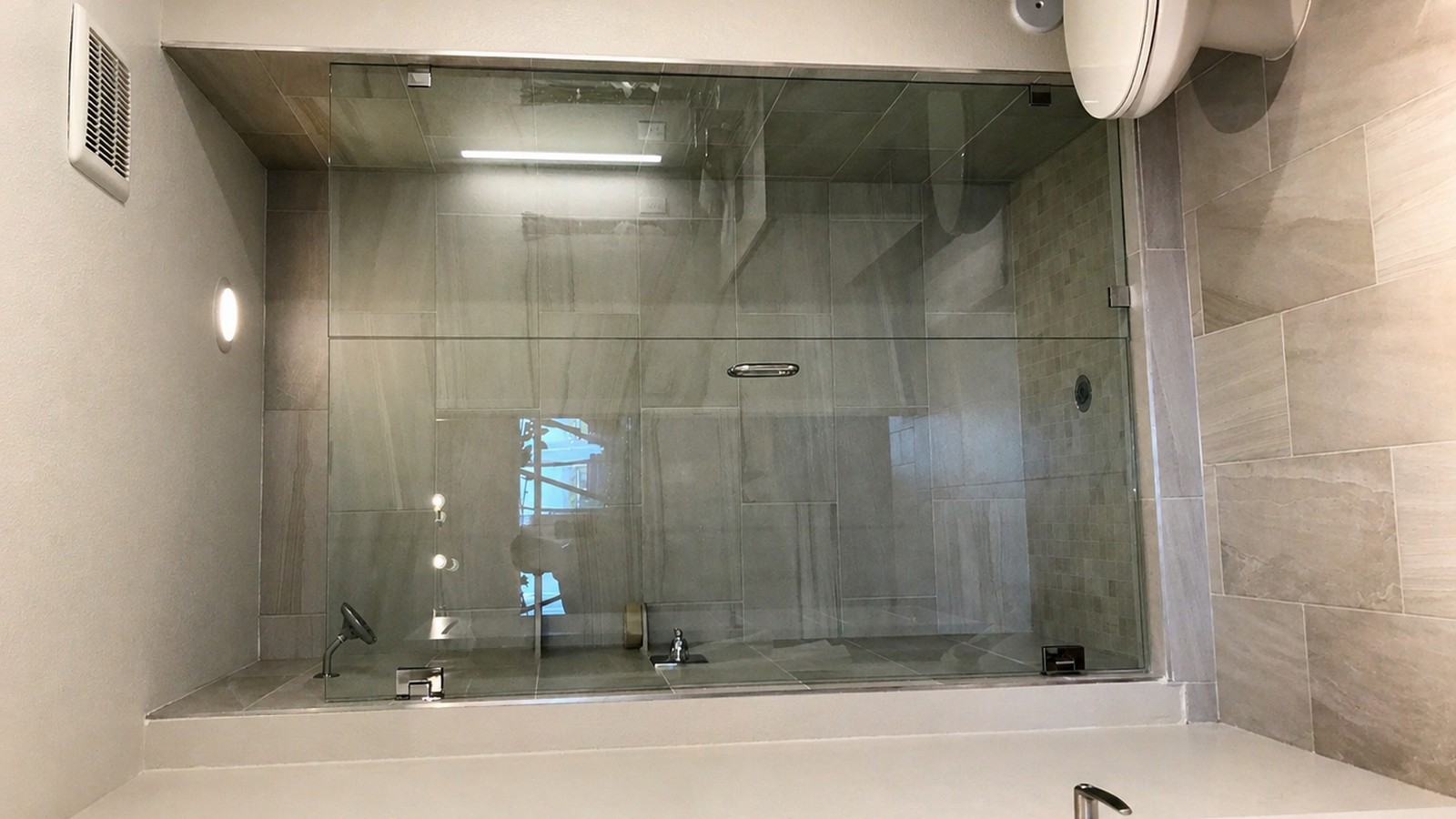 Frameless-glass walk-in shower with neutral porcelain tile, integrated tub deck, and folded towels — finished primary bath.