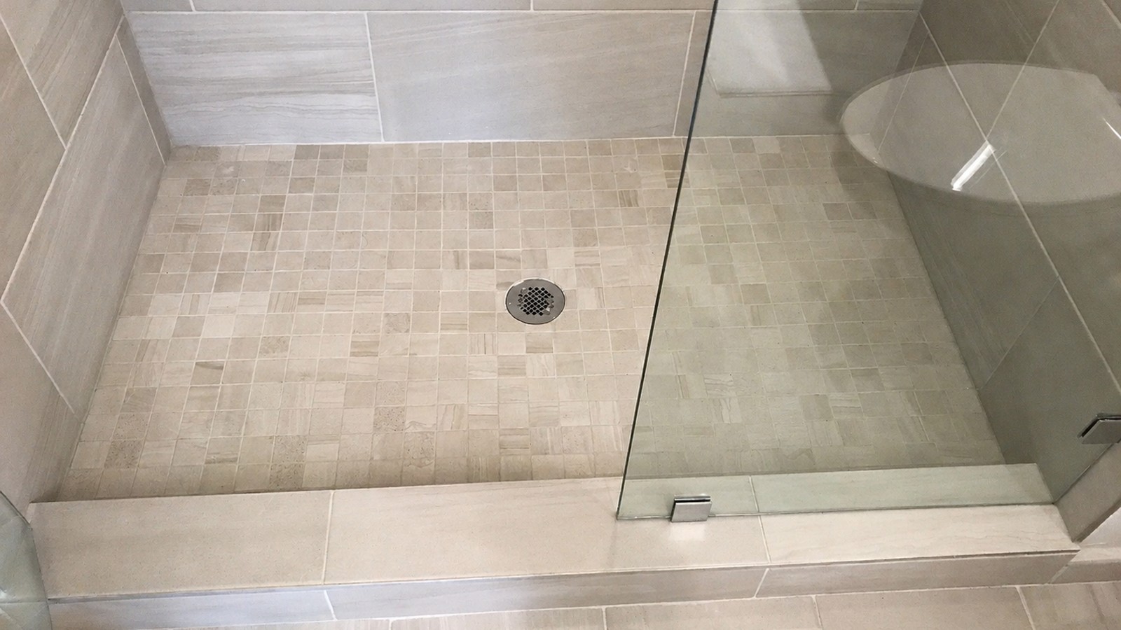Curbless shower entry with mosaic floor tile, center drain, and flush threshold to large-format adjacent tile.
