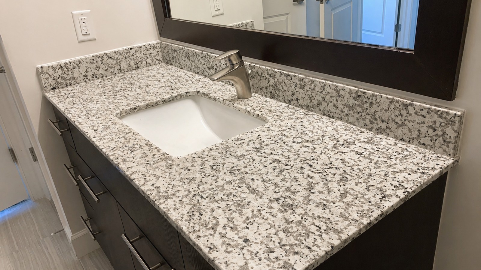 Bathroom vanity with white-and-grey speckled granite countertop and dark espresso-stained Shaker cabinets, undermount sink and brushed-nickel faucet.