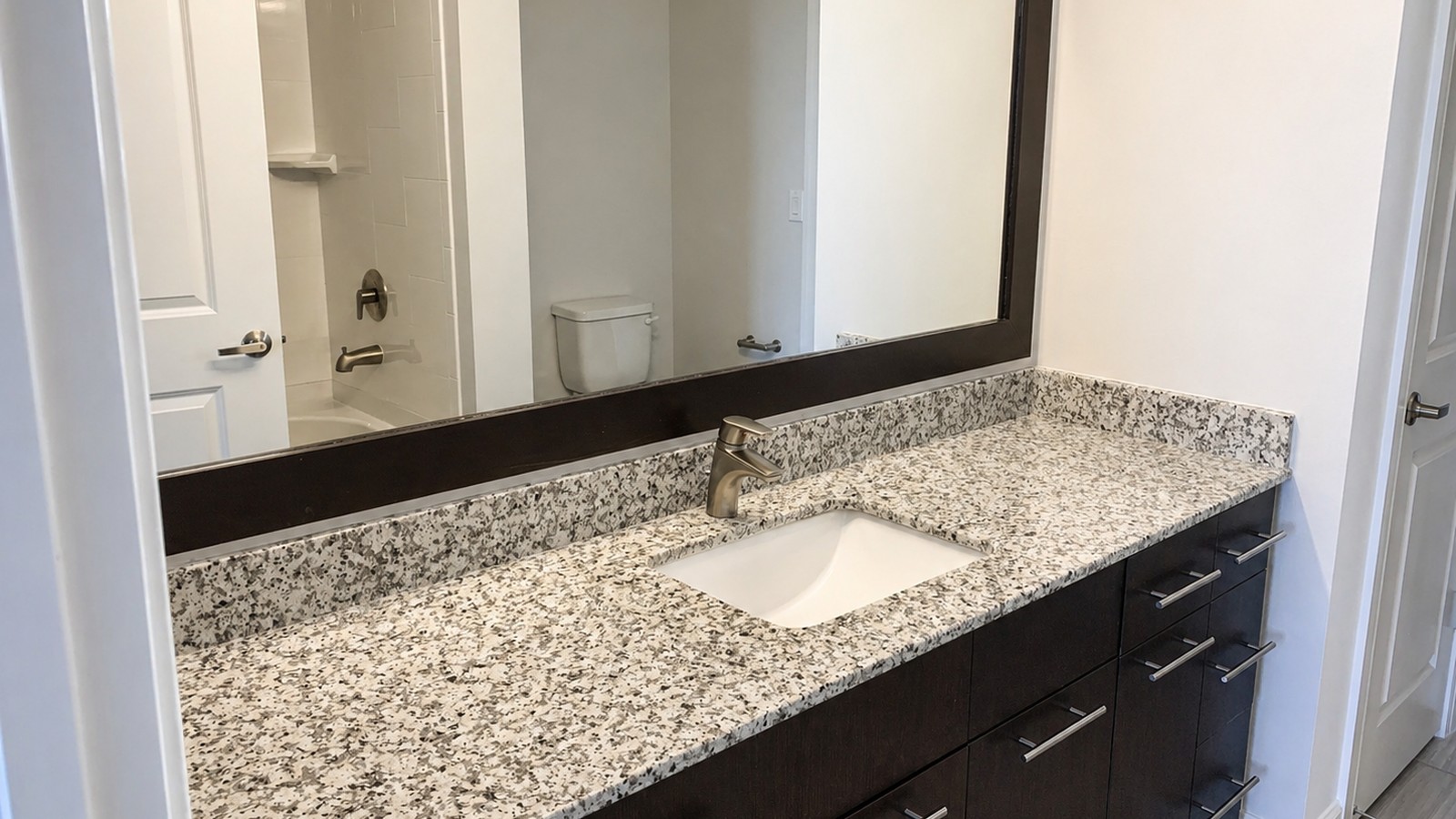 Finished primary bath: speckled granite top on espresso flat-panel vanity, undermount square sink, brushed-nickel single-hole faucet, framed mirror.