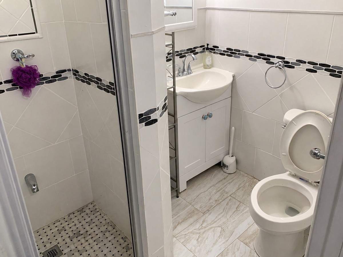 Finished bathroom with white tile, black-and-grey mosaic accent band, shaker vanity with chrome faucet, and glass-enclosed shower with basket-weave floor.