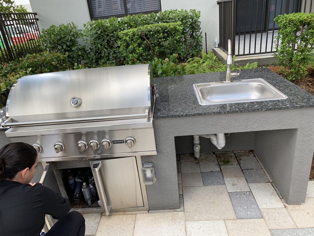 Built-in stainless Coyote-brand grill and prep sink set into a paver patio with black-granite countertop.