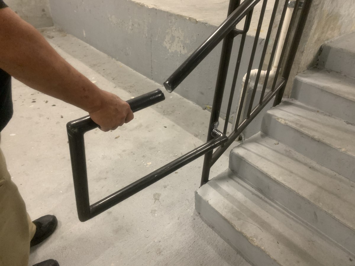 Installer test-fits a custom-bent steel pipe handrail extension at the base of an exterior concrete stair, prior to anchor.