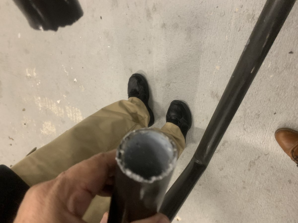 Cut end of black-painted steel handrail tube held next to the existing rail to confirm pipe diameter match.