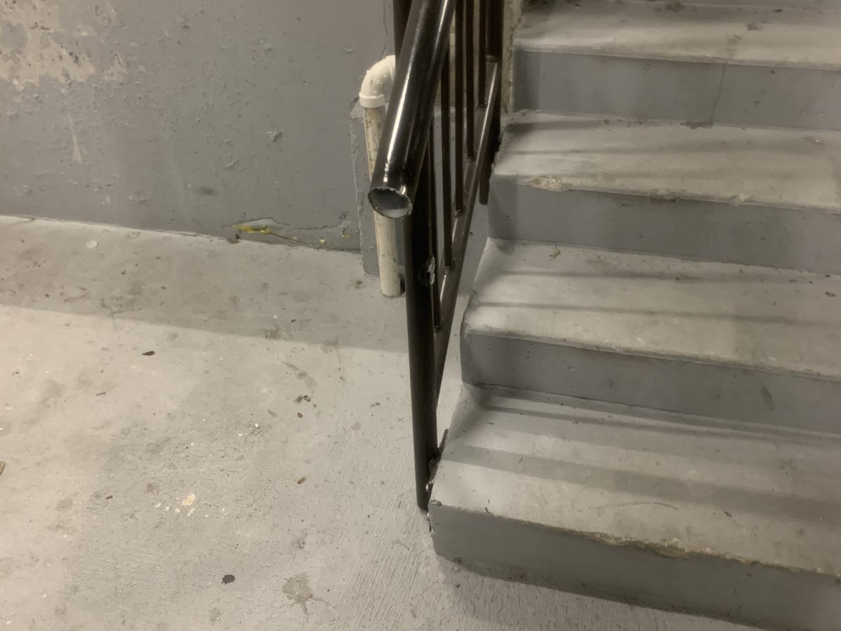 New black steel handrail anchored to concrete stair, with cut-and-bent extension landing prepared for welding.