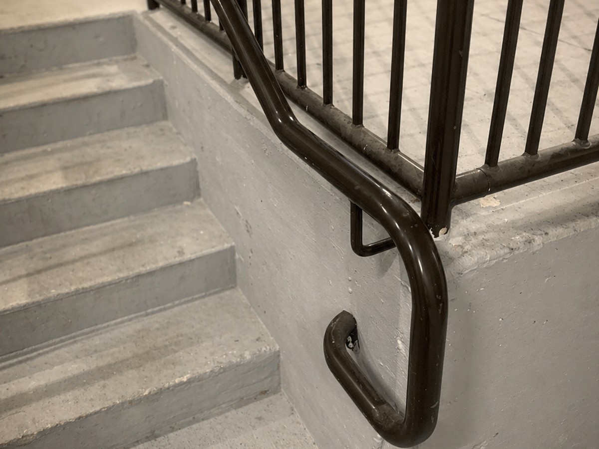 Finished black-painted steel handrail with looped bottom return securely wall-mounted at exterior concrete steps.