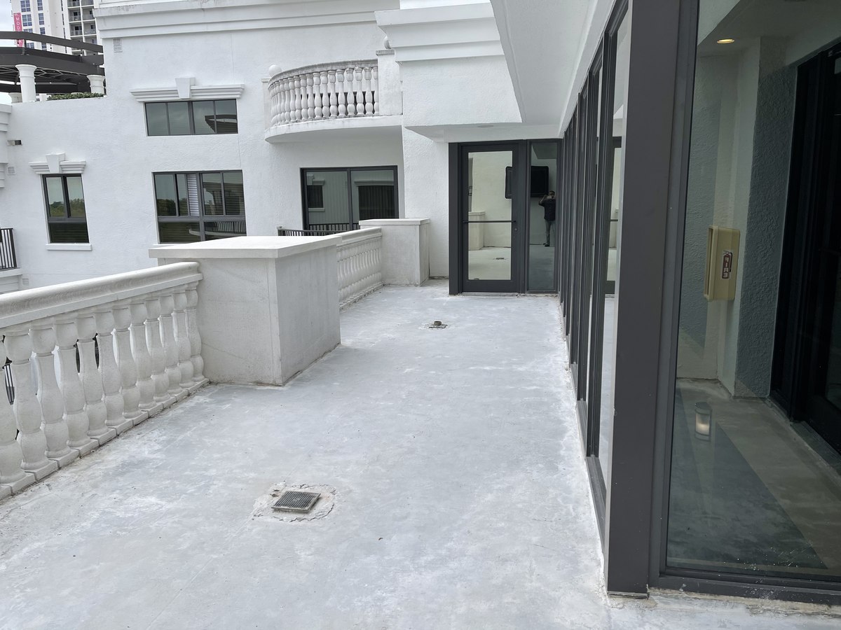 Newly waterproofed condo balcony with grey membrane, classical balustrade, and aluminum sliding-door system installed.