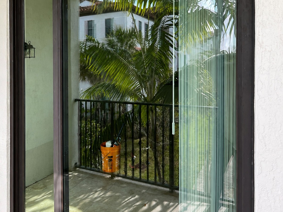 Layered glazing detail of a tall impact-rated slider, edge fins visible, condo terrace beyond.