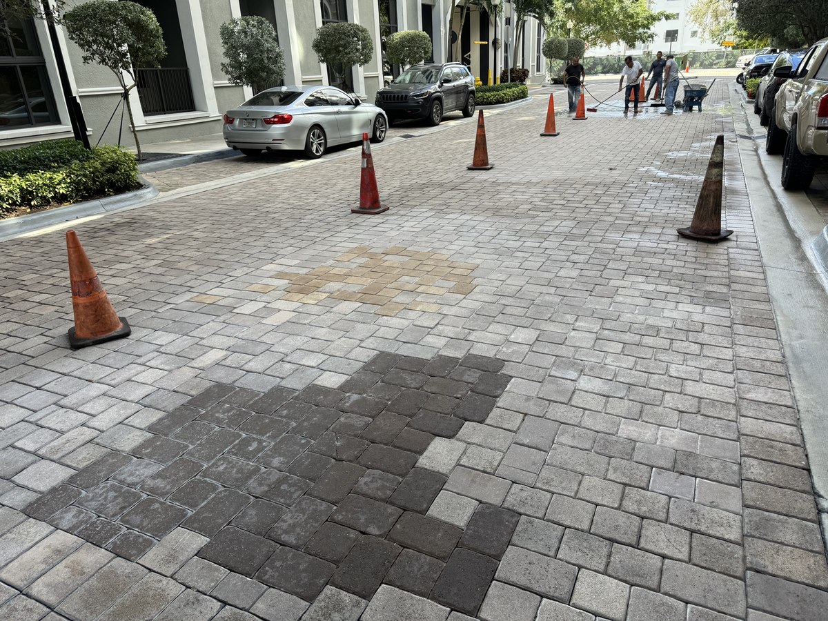 Paver patch in progress with traffic cones marking work zone, mismatched temporary pavers indicate sequenced repair.