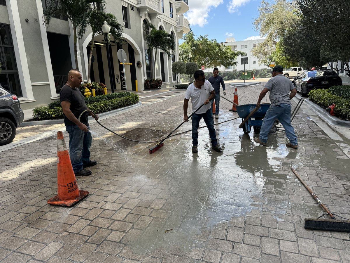 Five-person crew with squeegees and brooms washes new pavers after install on a Coral Gables residential drive.