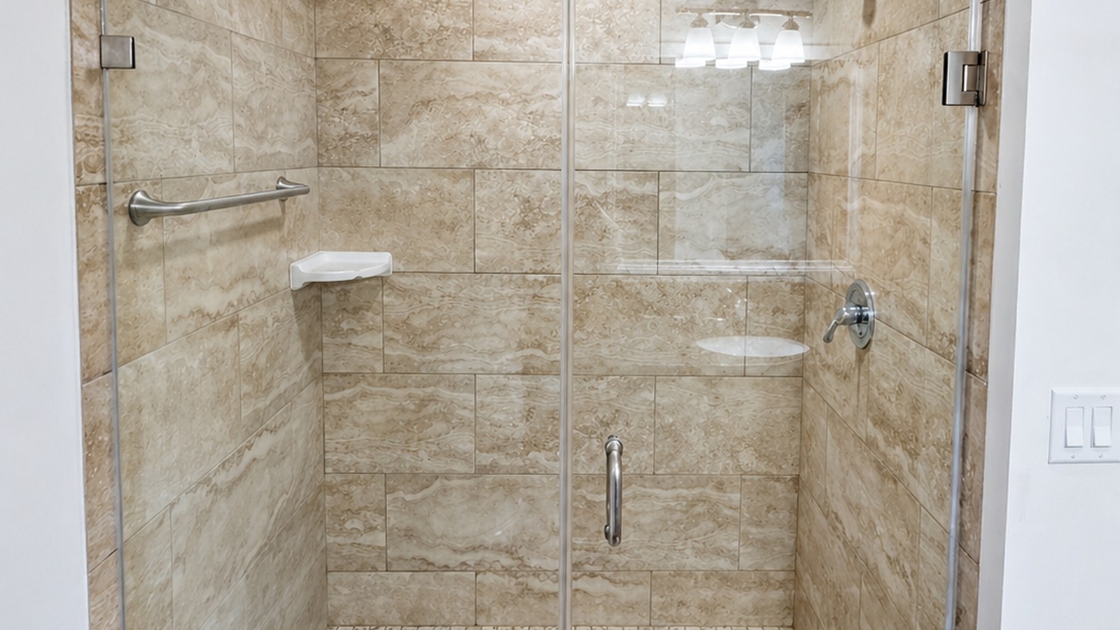 Frameless-glass walk-in shower with travertine-look porcelain walls, mosaic floor, and brushed-nickel hardware.
