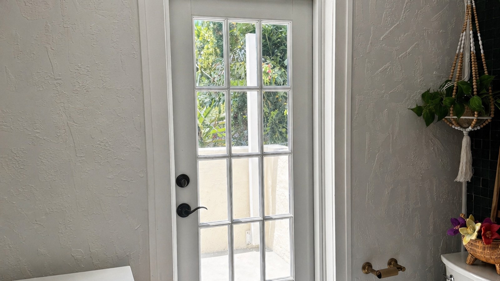 Bathroom with full-height French exterior door, stucco walls, dark teal subway accent, and white hex floor — finished primary bath.